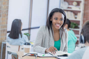 Two teens sitting across from each other at a small table with notebooks open in front of them