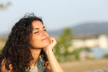 Teen girl with her eyes closed resting her chin on her palm outdoors