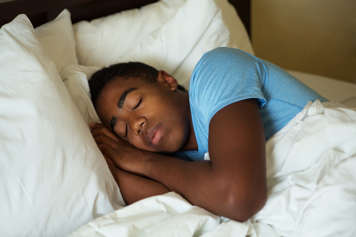 Teen boy sleeping on his side in bed with his hands up by his face on his pillow